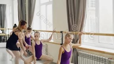 勤奋的年轻芭蕾舞演员正在做芭蕾舞和击球练习，而他们的女老师正在纠正错误